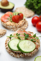 Crunchy buckwheat cakes with prosciutto, cucumber slices and greens on white table, closeup