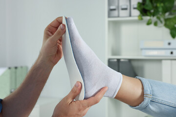 Male orthopedist fitting insole to patient's foot in hospital, closeup