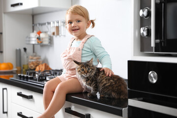 Cute little child sitting with adorable pet on countertop in kitchen