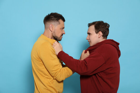 Two emotional men fighting on light blue background
