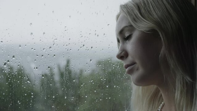 Depressed teenage girl leaning head against window on rainy day / Cedar Hills, Utah, United States
