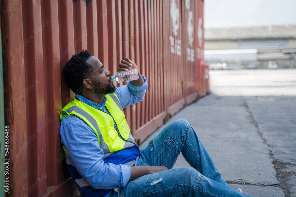 Poster Worker sitting to rest with container wall in background.