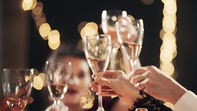 Happy festive group of friends drinking alcohol celebrating Christmas New Year waving sparklers. Close up hands cheers champagne clinking glasses. Smiling multiethnic people at Christmas eve night.