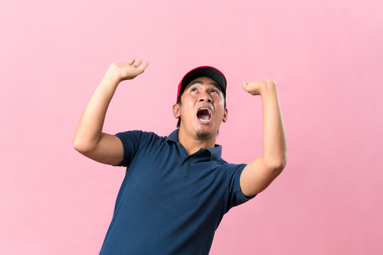 Delivery man in uniform attempts to hold something heavy from above, isolated on a pink background.