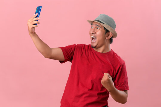 Young Asian man holding smartphone doing winning gesture holding mobile phone, Happy get special gift online