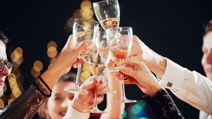 Happy festive group of friends drinking alcohol celebrating Christmas New Year waving sparklers. Close up hands cheers champagne clinking glasses. Smiling multiethnic people at Christmas eve night.