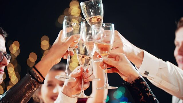Happy festive group of friends drinking alcohol celebrating Christmas New Year waving sparklers. Close up hands cheers champagne clinking glasses. Smiling multiethnic people at Christmas eve night.
