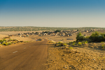 Empty high road or national high way approaching remote desert village inside the desert. Distant horizon, Hot summer at Thar desert, Rajasthan, India.