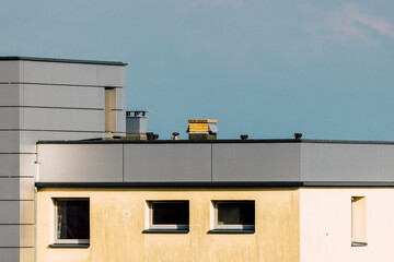 Rooftop of a modern city building with metal cladding, yellow chimney and blue sky