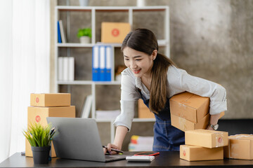 Happy woman selling products online Started as a small SME owner using a laptop computer on a table with parcels of mail in her room.