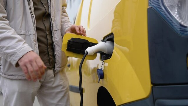 Male hand inserts power connector into cargo EV car. Electric car charging concept