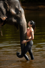 Beautiful girl model with sporty body posing hugging elephant in the river, Kanchanaburi, Thailand. 