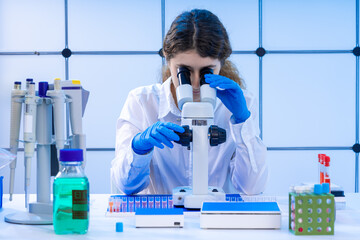 young adult female student working with a microscope examining biological samples using a...