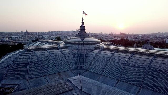 Drone view of French flag waiving at the top of The Grand Palais, a castle of glass at sunrise in Paris, with forward drone motion