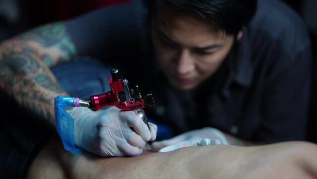 Professional tattooist makes the tattoo on a men waist, focusing on tattoo machines in a modern studio low light.