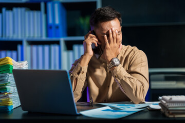 Overtime work concept, Handsome asian business man working late at night in office workplace. Mobile calling. Feeling sad.