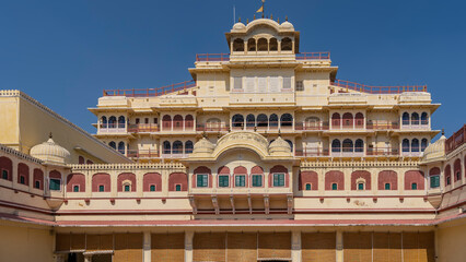 Fototapeta na wymiar An ancient palace complex in Jaipur against the blue sky. The sandstone building is decorated with arches, carvings, decorative lattices, terraces, balconies, spires. India