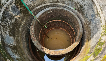 Fototapeta na wymiar Undrinkable and unhygienic bad muddy contaminated brown or yellow color dirty drinking water inside old african damaged well. Drought, less rainfall, shortage, scarcity and crisis in Africa concept.