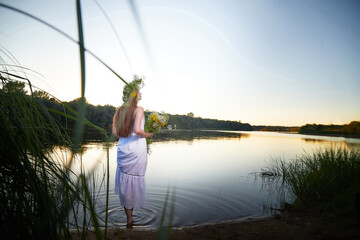 Portrait of beautiful slavic girl with long hair with flower crown in a water of river or lake on nature in warm evening. National selebration of summer holiday of Ivan Kupala
