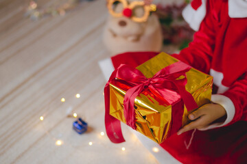 Girl's hand holding a golden gift box with red ribbon for Christmas and New Year.