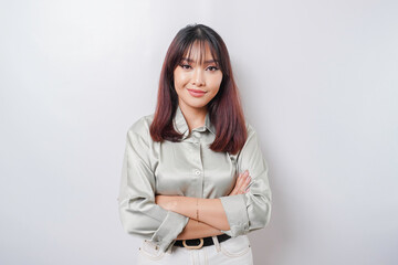Portrait of a confident smiling Asian woman wearing sage green shirt standing with arms folded and looking at the camera isolated over white background