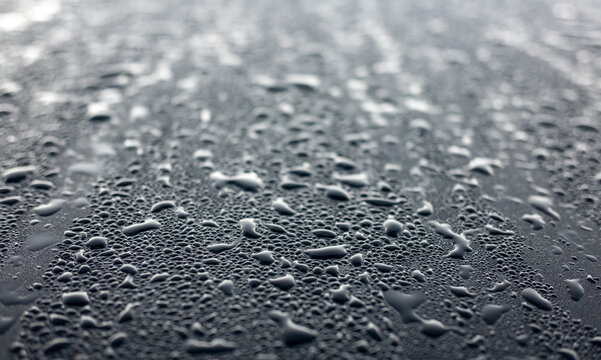 Dew drops on the black hood of a parked car. Background