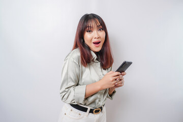 Naklejka premium Shocked Asian woman wearing sage green shirt and holding her phone, isolated by white background