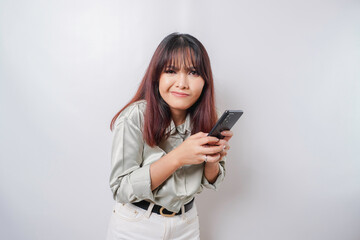 Fototapeta premium A dissatisfied young Asian woman looks disgruntled wearing sage green shirt irritated face expressions holding her phone