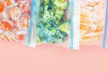 Three packages with frozen vegetables on pink background, top view