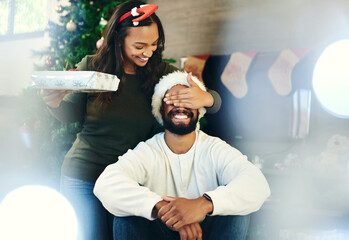 Christmas, bonding couple and surprise gift in house or home living room for holiday celebration, love or festive vacation. Smile, happy or xmas woman with present box in morning secret santa for man