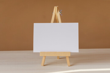 White blank sheet of paper with place for copy space on wooden easel stand. Close-up, white-brown...