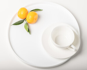 A white empty cup on a white dish and two tangerines.