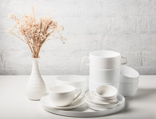 Stacks of white dishes and a bouquet of dried flowers on a white table. Scandinavian minimalism.