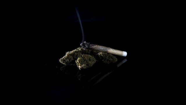 Burning cannabis joint and medicative weed buds on black background with smoke