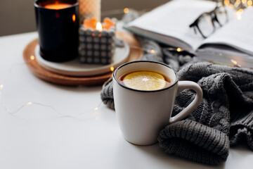 Winter home cozy concept.Cup of tea with lemon, open book, warm sweater, candles and fir tree....