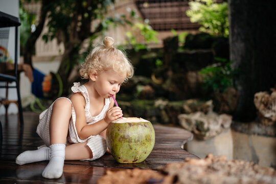 Healthy and wholesome food. A child drinks fresh coconut through a straw while sitting on the terrace of his house in the summer on vacation.