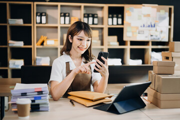 Portrait of Asian young woman SME working using smartphone or tablet taking receive and checking...