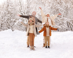 Happy family father, mother and kids throwing snow in air, rejoicing winter on snowy day in nature