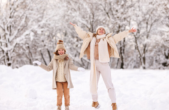 Happy family mother and daughter rejoicing first snow in snowy winter park