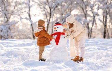Fototapeta na wymiar Cute little boy making snowman with mom in winter park