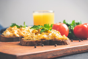 Scrambled eggs with parsley on bread, homemade healthy breakfast on dark wooden board