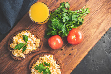 Scrambled eggs with parsley on bread, homemade healthy breakfast on dark wooden board, top view