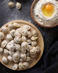 Traditional Russian dumplings with meat on a black wooden background, ingredients, flour, eggs, salt, pepper, Russian national cuisine dish, top view, frozen semi-finished product.