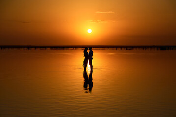 Couple with a bouquet on a pink lake. Sunset and reflection in the water