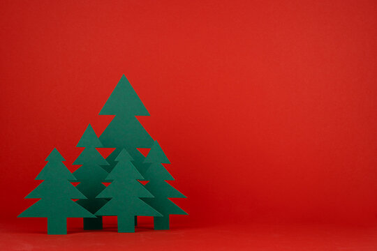 Bright Christmas background with paper green spruce forest on red backdrop in minimalist modern style, copy space. New year scene for presentation products and advertising text, card, poster, flyer.