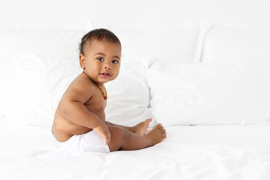 Baby boy in diaper sitting on white bed wearing amber teething necklace