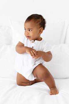 Baby boy kneeling on white bed looking away