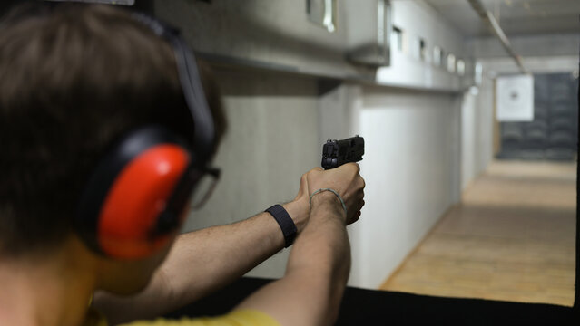 Man in tactical headphones aiming gun at target in shooting range