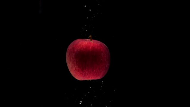 Slow motion one red apple falling into transparent water on black background. Beautiful fresh fruit splashing in aquarium. Organic fruits, healthy food, diet, air bubbles