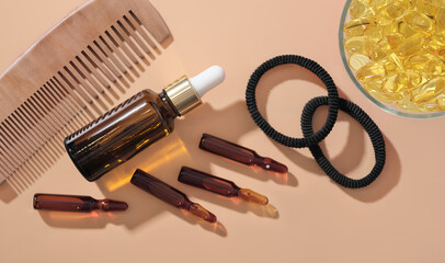 Hair growth ampules and serum solution next to omega 3 capsules and wooden comb on beige background. hair care medical treatment . top view